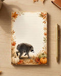 A lined notepad with an autumn-themed Jimothy the raccoon illustration on the cover, styled on a wooden desk with fall leaves, a pen, a mug, and a leather notebook.