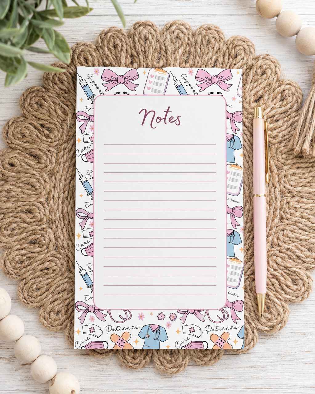 A decorative nurse themed notepad with lined writing space and the word 'Notes' at the top, styled on a braided jute placemat with a pink pen beside it on a white wood surface.
