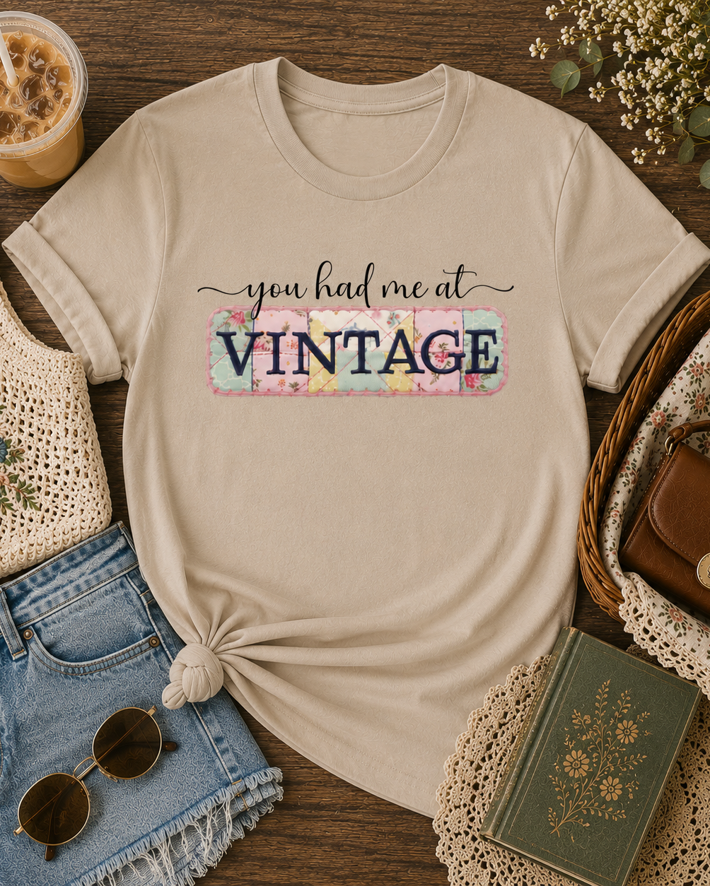 Sand Shirt with “You Had Me at Vintage” graphic tee styled in a cozy flat lay with iced coffee, denim shorts, sunglasses, crochet accessories, and vintage-inspired thrifted finds.